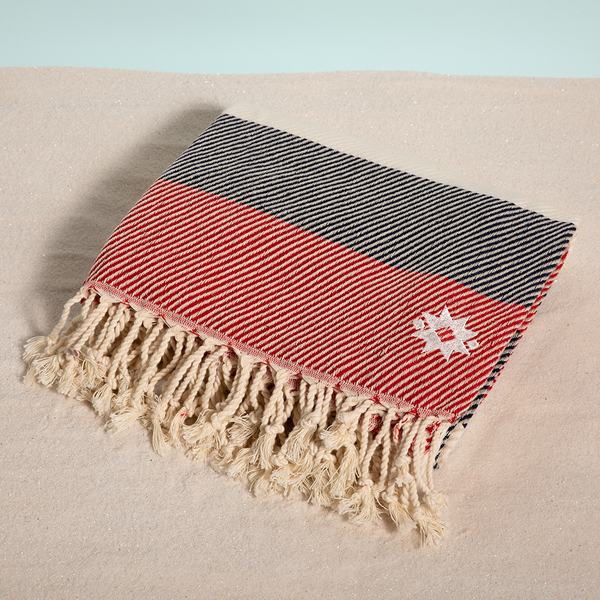 Anchors Away keyf Turkish beach towel folded with logo on sand