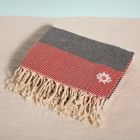 Anchors Away keyf Turkish beach towel folded with logo on sand